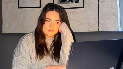 Chloe Chloe with long dark brown hair working on a laptop