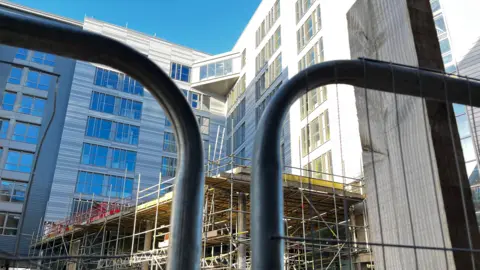 Scaffolding is outside the hotel building, which is behind a black barrier.