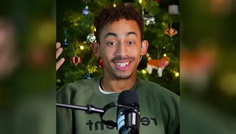 Jordan Stephens smiles in front of Christmas tree