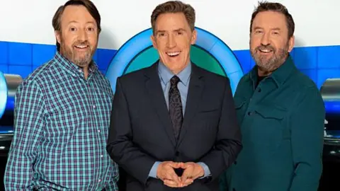 BBC / Zeppotron / Brian Ritch Comedian David Mitchell dressed in a shirt, show host Rob Brydon smiling and dressed in a suit and another comedian Lee Mack dressed in a shirt for a promo shot for BBC hit TV show Would I Lie To You