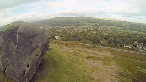 Sebuah batu besar, pemandangan perbukitan di atas Bradford dan awan-awan yang indah. 