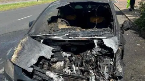 A burnt-out car on the side of a road