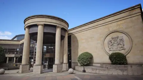 PA Media High Court in Glasgow is a sandstone building with columns by the entrance and a crest on the wall