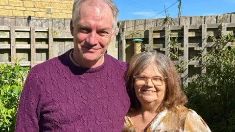 Husband and wife, Mark and Jan Taylor stand together in their garden.