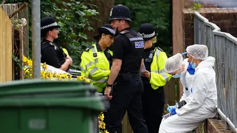 Six police officers are at the scene. Two are wearing hi-vis jacket, another two are wearing police uniform, and two are wearing white boiler suits.
