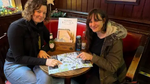 University of York Victoria Wells (L) and Nadine Waehning (R) sat at a table at what looks like a pub, smiling and pointing at the map