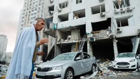 EPA Injured man in a blue blanket standing outside a damaged building