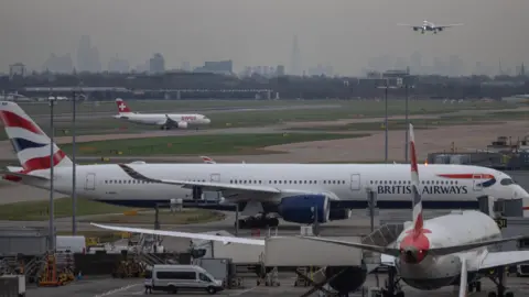 Reuters Planes on a runway with another plane in the background coming into land.