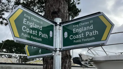 George Carden/BBC Metal signs which read King Charles III England Coast Path public footpath