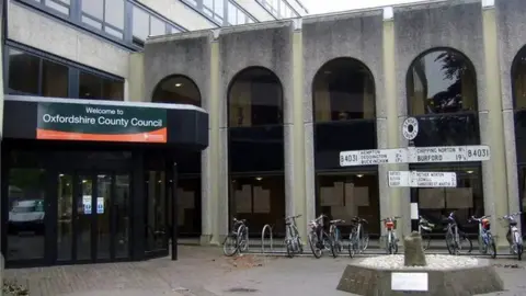 Concrete building with revolving doors at entrance and bicycles lines up along a wall a post sign stands on a concrete plinth