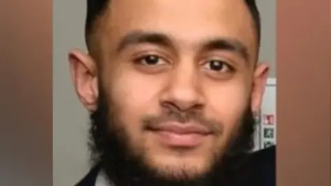 Family handout A man wearing a suit and pink tie looks at the camera. He has black hair and a thick beard.