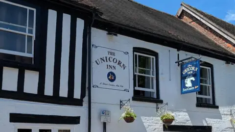 Neil Ainsworth The outside of a pub with the words The Unicorn Inn on the mainly white front and also with The Unicorn Inn words on the blue sign at right angles to it.