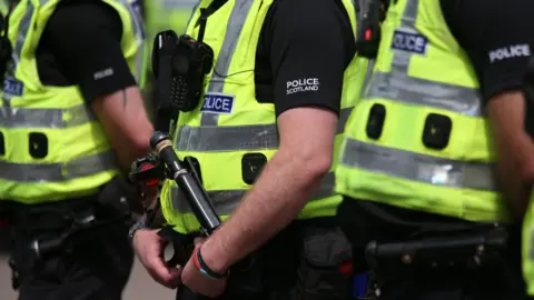 PA Media Three police officers standing in a row, all are wearing Hi-vis vests and black uniform