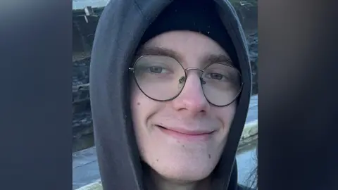 Hampshire Police Taylor Connors smiles at the camera, wearing a grey hoodie and round glasses that are not quite circular.