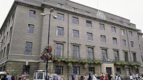 The Guildhall in Cambridge, a grey building with hanging baskets beneath a first floor balcony