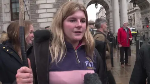 Molly Saville wearing a blue and pink shirt holds a banner during the march in London