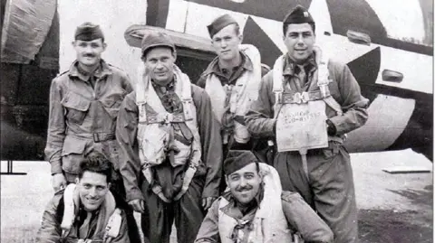 A black and white photo of US aircrew dressed in caps and flying attire posing for the camera in front of an aircraft.