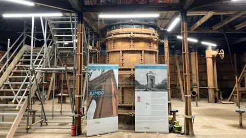 Jodie Halford/BBC Scaffolding, metal stairs and a large cast-iron pipe are pictured around an industrial-looking room with a very high ceiling.