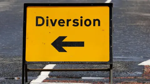 A yellow sign in a road with black writing and an arrow that reads "diversion"