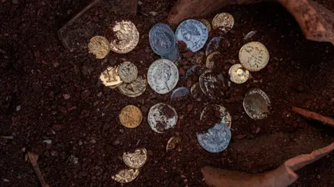 The image shows some silver coins in the first, with a broken earthenware pot in the background.