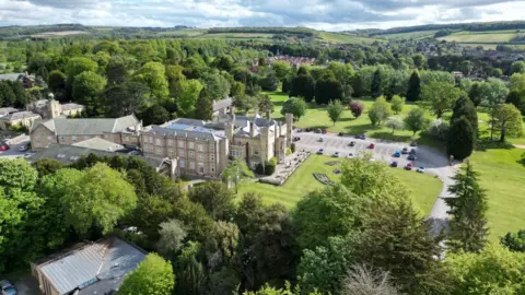 Joe Bilton / BBC A drone shot of Cave Castle. A castle-like building is surrounded by greenery. 