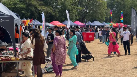 People flock to the stalls around the sides of the festival, selling various goods.