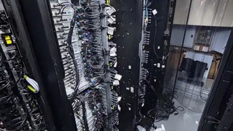 City of London Police A row of computer servers, tall stacked black computer cabinets with multiple trays and wire connections