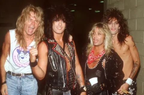 Getty Images Rock band Motley Crue pose backstage at a concert, sporting shaggy 80s hairdos and a variety of leather-studded clothing, except for drummer Tommy Lee Jones, who is shirtless
