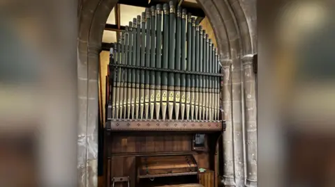 All Saints Church An organ under an arched stone wall, with its pipes mirroring the shape of the archway.
