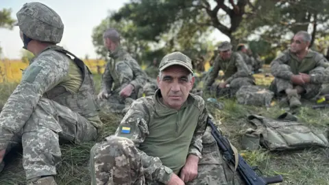 Rostyslav in uniform on a field surrounded by other Ukrainian recruits