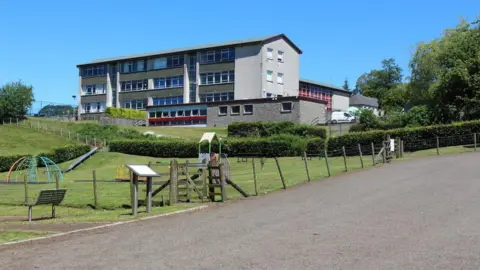 Graham Robson/ Geograph A three-storey municipal building at the top of a hill. On the lawn leading up to the building is a children's playpark