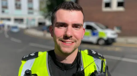 Sergeant Kemish is wearing a yellow reflective jacket and police body camera