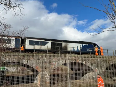 A train with scorch marks on the outside from a fire is inspected by Network Rail staff