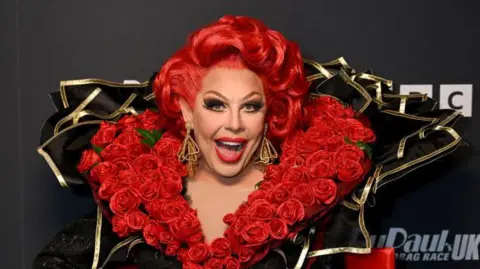 A woman with red hair and many red roses around her neck. 