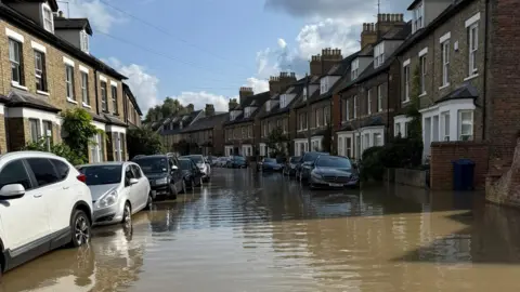 A street in Oxford with water reaching the base of most cars parked on either side.