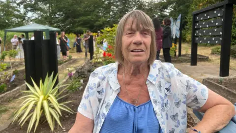 A woman with a blue top smiling into the camera she has got a white blouse on underneath.