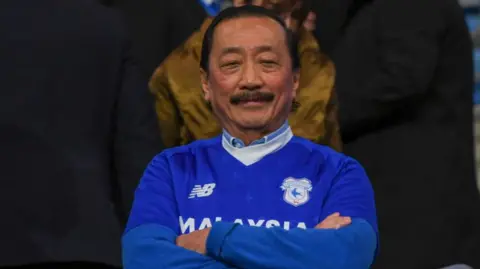 Owner Vincent Tan sits with arms folded in a Cardiff City shirt