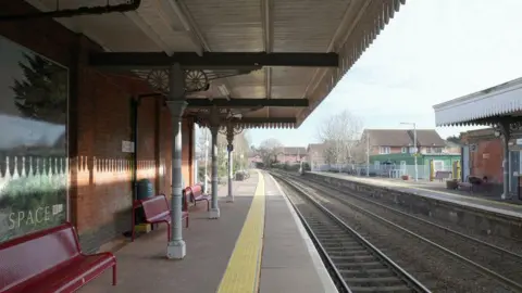 Empty platform and railway tracks. Red benches against a platform building wall.