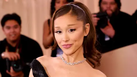 Ariana Grande poses for the cameras at the Golden Globes earlier this year. She is wearing a black dress and diamond necklace and has her hair in a ponytail.