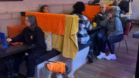 Liam Downey Several booths full of people talking to each other over cups of tea or playing connect four.