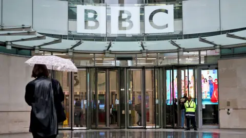 A person walks with an umbrella outside BBC Broadcasting House in London in November 2025
