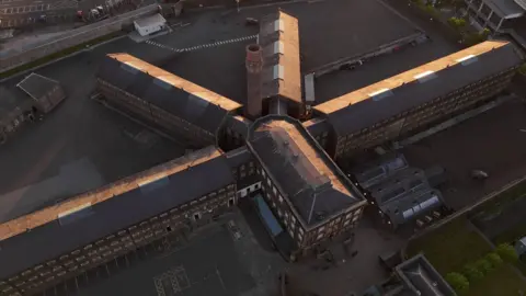 An aerial drone image of the former Crumlin Road jail which consists of a large central block with four long wings radiating from it.