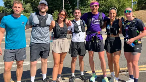 Seven runners are lined up on a pavement and smiling for a photo.