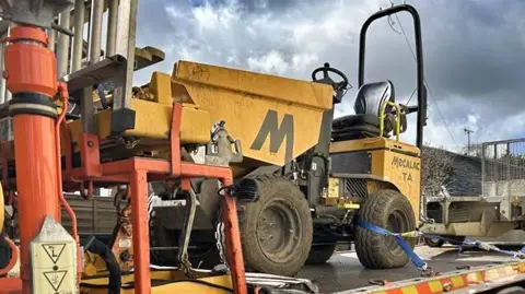 Construction equipment and a small vehicle on a trailer.