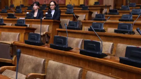 EPA Empty seats in the Serbian parliament, and microphones on the desks above them 