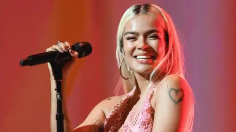 Colombian singer Karol G holds a microphone and smiles as she performs at a concert in Los Angeles 