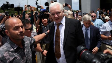 Julian Assange is led through a group of journalists outside court