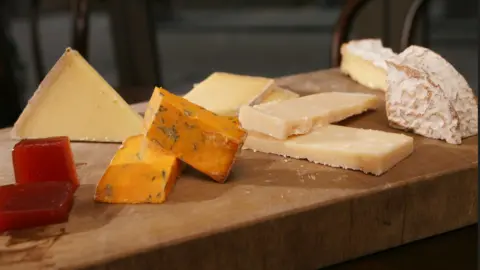 A wooden block with a variety of different cheeses laid out