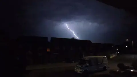 Thomas Pugh A bolt of lightning strikes behind some homes on a residential estate during the night.