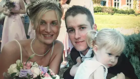 Family photo Sarah and Shaun on their wedding day with their daughter. Sarah is wearing a tiara with her hair up and a bouquet of flowers.